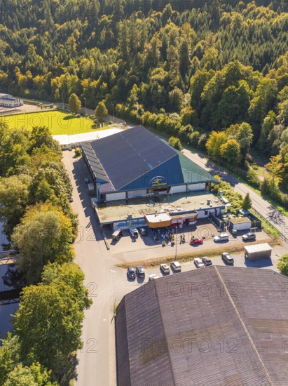 Industrial building in the forest next to a road, large car park, shady areas, green surroundings,