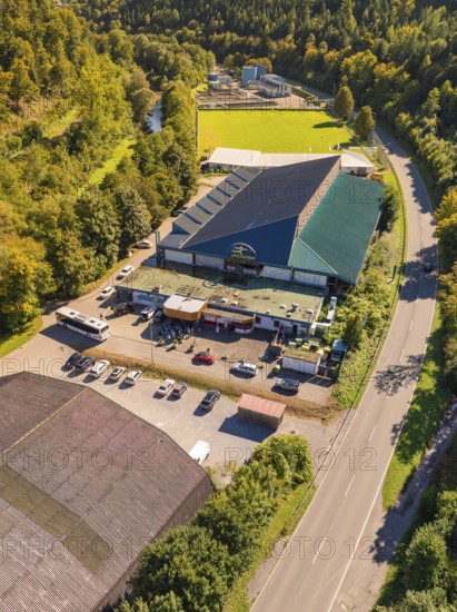 Industrial building with adjacent car park and green landscape, light roof colour, surrounded by a