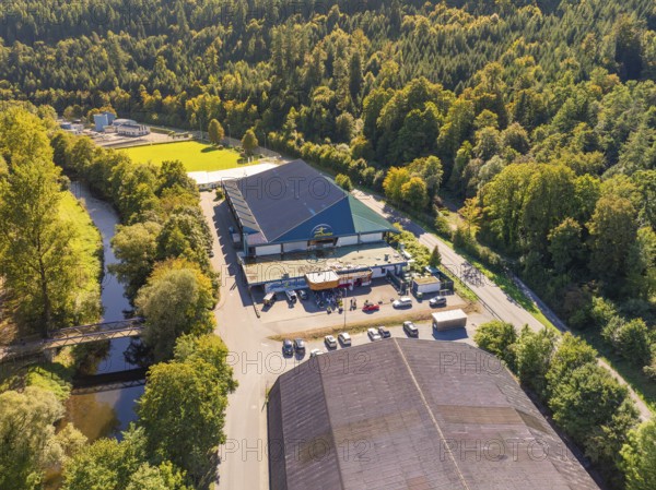 Large building in wooded surroundings near a river, well-frequented car park, bright daylight,