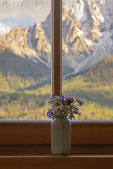 A vase with meadow flowers stands on the windowsill in the background the mountains of the