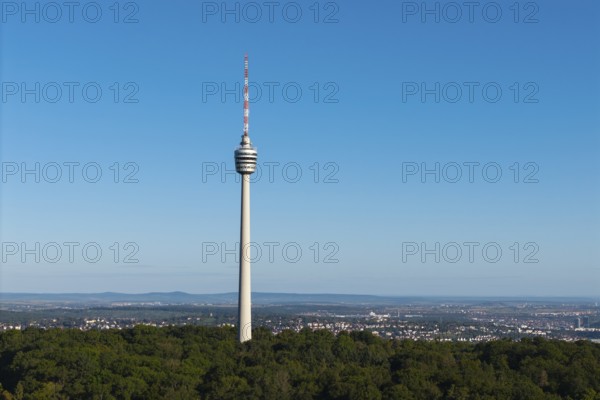 Detailed view of a television tower, embedded in forests, with a wide view of the city under a blue