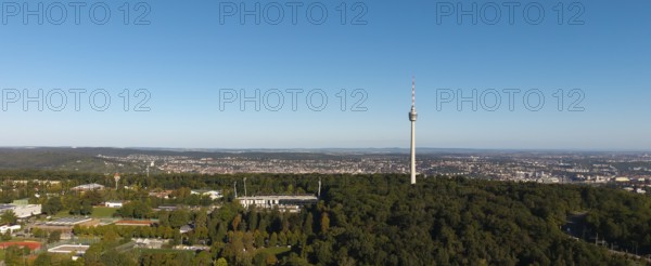 Panoramic view of a cityscape dominated by a television tower and surrounded by dense forests under