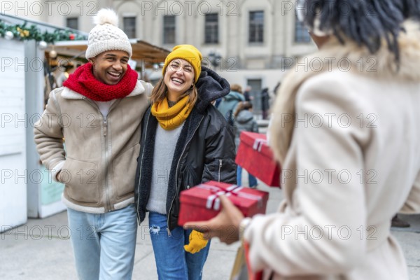Friends laughing and exchanging christmas gifts at a winter market in the city, enjoying the