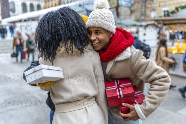 Two friends joyfully exchanging gifts at a bustling outdoor christmas market, surrounded by festive