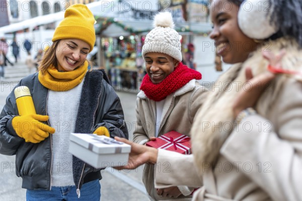 Happy multi ethnic friends exchanging christmas gifts at an outdoor winter market, enjoying the