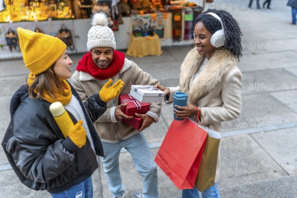 Happy multi ethnic friends exchanging christmas gifts and enjoying hot drinks at a winter christmas