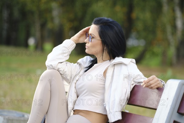 A woman with long dark hair sits on a park bench, dressed in comfortable attire. She gazes