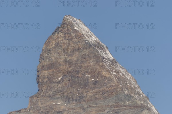A towering Matterhorn mountain peak stands prominently against the clear blue sky, revealing rocky