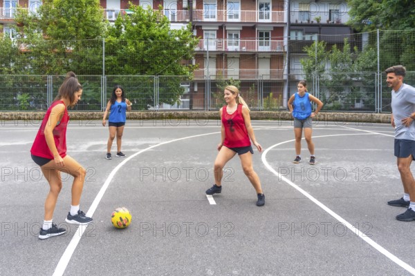 Female soccer players in red and blue jerseys kicking a yellow soccer ball during a friendly