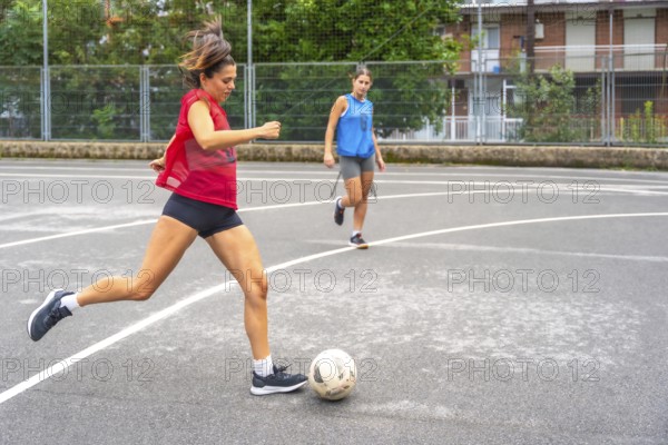 Two women athletes playing soccer on an outdoor court are passing the ball to each other,