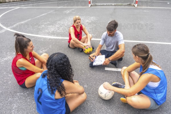 Soccer coach sitting on the field, drawing game strategy on a clipboard while female players listen