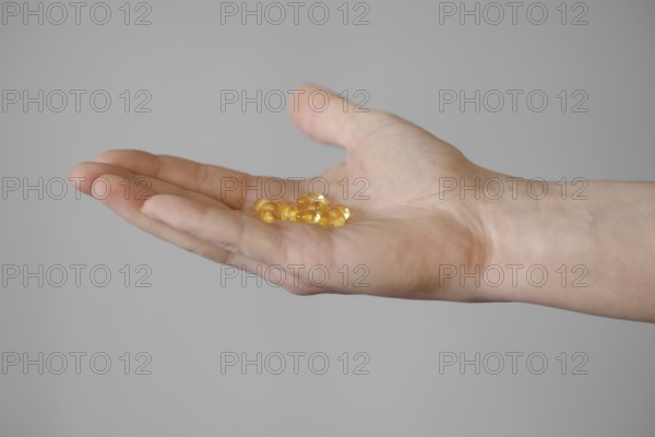 A person extends a hand, showcasing multiple yellow capsules resting on their open palm. The