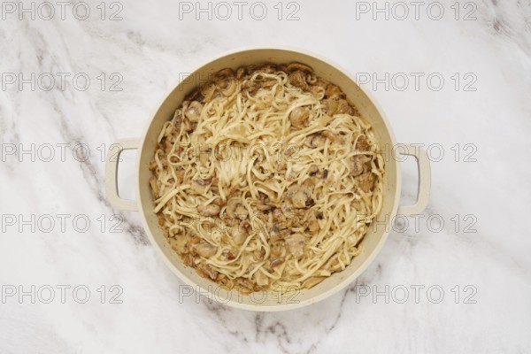 Overhead view of double handled pot with cooked noodles and creamy mushroom sauce on a marble