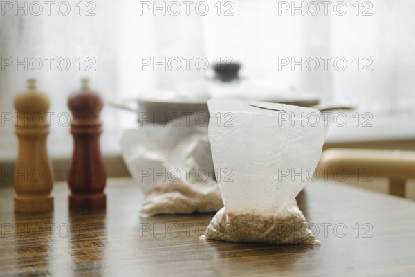 Pearl barley is prepared for cooking in convenient sachets placed on a wooden table. Nearby, salt