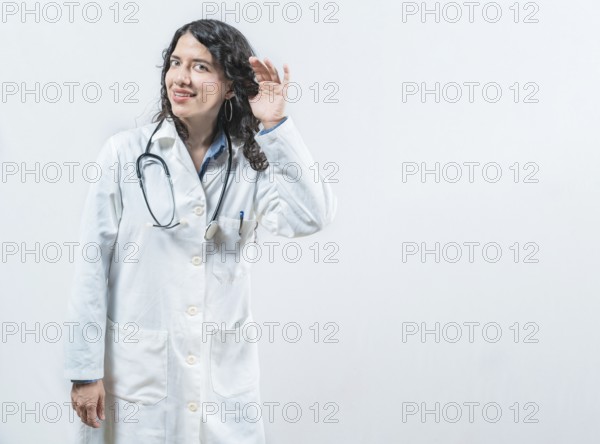 Latin female doctor listening to gossip, looking at camera. Doctor with hand on ear listening to