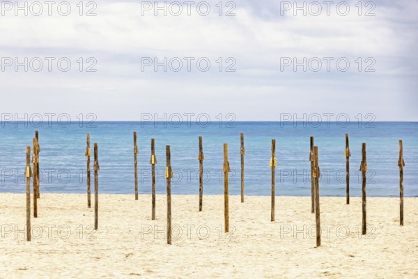 Parasol poles on a empty sandy beach by the Mediterranean sea with a seascape view to the horizon,