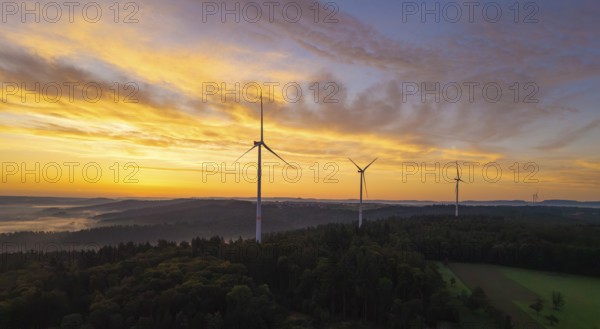 Wind turbines above a rich forest landscape at sunrise with a yellow pastel sky, near Schorndorf,