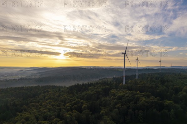 A row of wind turbines overlook a wooded area as the morning fog lifts, near Schorndorf, Rems-Murr