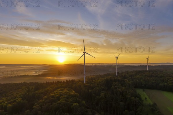 Three wind turbines at sunrise with a golden sky over a forest landscape, near Schorndorf,