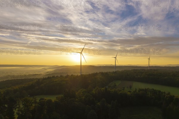 Three wind turbines above a hilly landscape, morning clouds reflecting the rising sunlight, near
