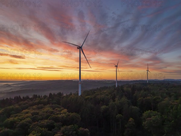 Wind turbines in the foreground of an intense pink-orange sunrise over a forest, near Schorndorf,