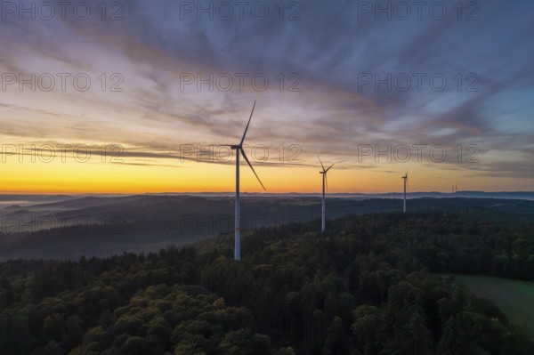 Three wind turbines on a wooded hill with a dramatic sunrise sky, near Schorndorf, Remstal,