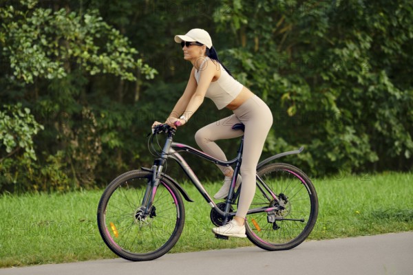 A woman enjoys riding her mountain bike along a serene path in a park. Dressed in fitted
