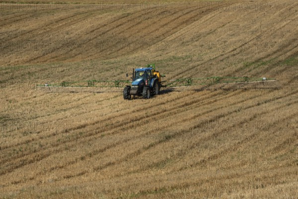 Tractor spreading fertilizer on harvested stubble field in Ystad municipality, Skåne county,