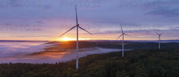 Powerful wind turbines over a misty forest and a wide horizon at sunrise, near Schorndorf,