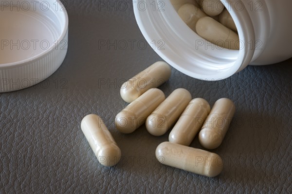 Open bottle with beige capsules and separate lid on one surface, food supplement, iron supplement,