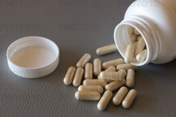 Open bottle with scattered beige capsules on a dark surface, food supplement, iron preparation,
