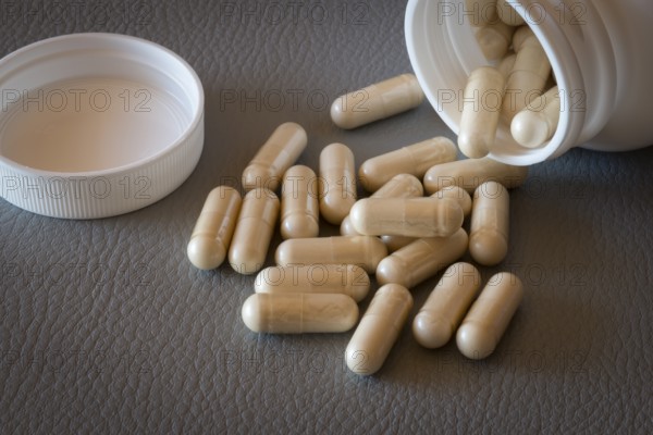 Beige capsules that have fallen from an open bottle with the lid removed onto a surface, food