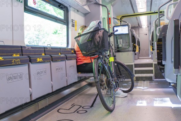 A cyclist sits in a modern, bright train compartment with his bicycle, battery Electric train with