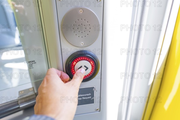 Hand operates a red illuminated stop button on a door in the vehicle, battery Electric train with