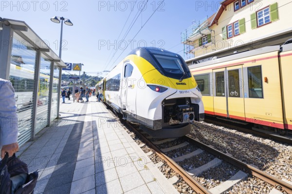 Modern yellow and white train at the station with green and red building in the background, battery