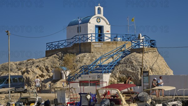 Small chapel on rocks with blue and white accents and blue roof, Chapel Agios Nikolaos, harbour,