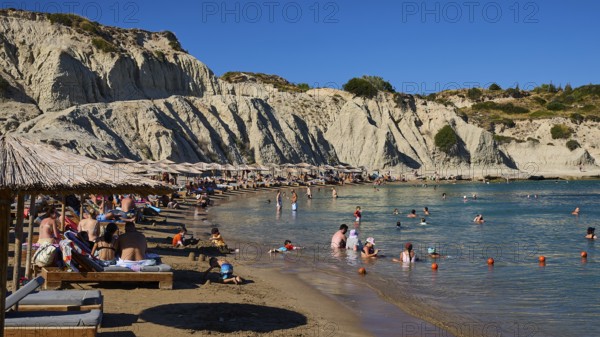 Pleasant scenery on the beach with beach loungers, bathers and magnificent rocky backdrop, Limanaki