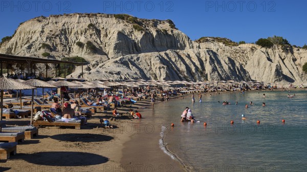 Long beach with sun loungers and bathers in front of an impressive rock face, Limanaki beach,