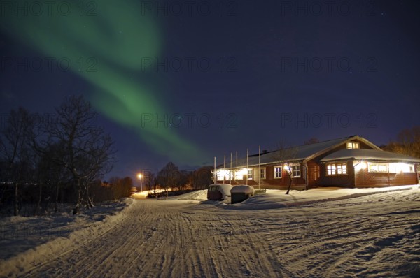 A snowy path leads to a house under the Northern Lights and a clear night sky, Sortland campsite,