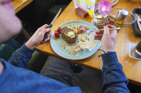 Person eating a dish in a restaurant, consisting of meat and tomatoes on a plate, Lake Constance,