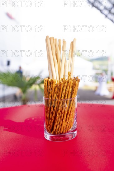 A glass container with breadsticks stands on a red table in an outdoor event area, Lake Constance,