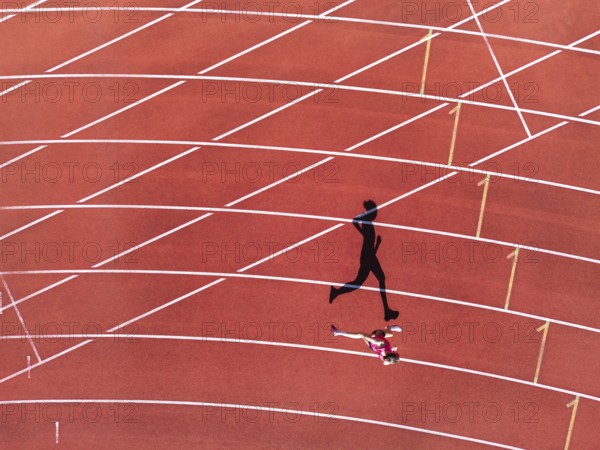 Aerial view of a female individual (runner) on a red athletics track (tartan track) with shadow as