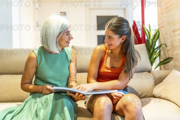 Smiling senior woman and young woman reading a book together on a comfortable sofa in the living