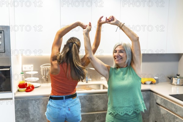 Two women joyfully dancing in a modern kitchen, embodying happiness and togetherness, surrounded by