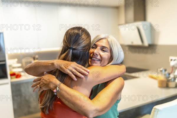 Happy senior woman embracing her adult daughter in a kitchen, enjoying a tender moment of affection