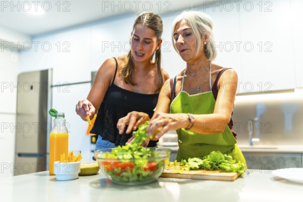 Mother and daughter preparing a mixed salad with lettuce, tomato, and orange juice in a modern