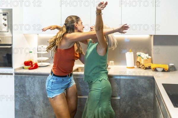Happy mother and daughter are dancing together in their modern kitchen, enjoying a carefree moment