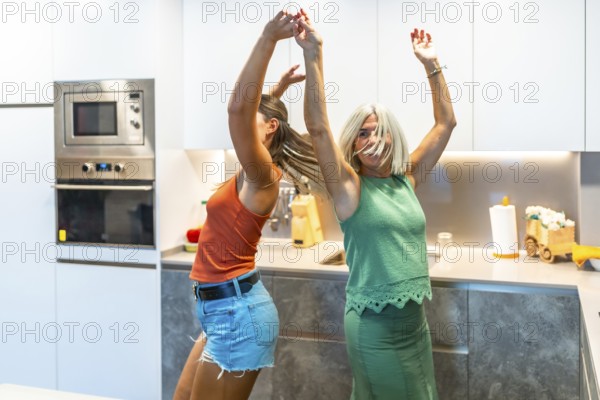 Two women enjoy a lively dance in a contemporary kitchen, celebrating happiness and friendship with