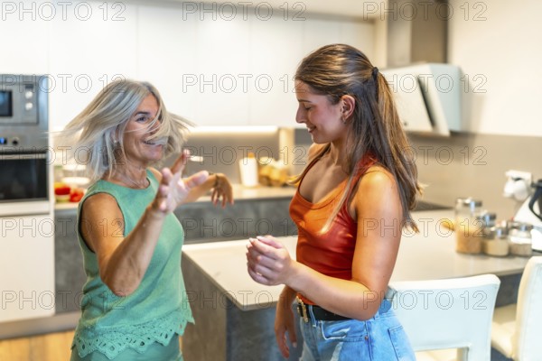 Happy mother and daughter are dancing together in their modern kitchen, enjoying a carefree moment