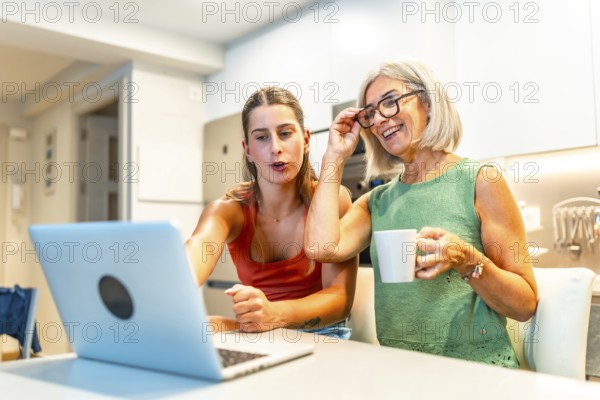 Happy mother and daughter enjoying online streaming content on a laptop while having a coffee in a